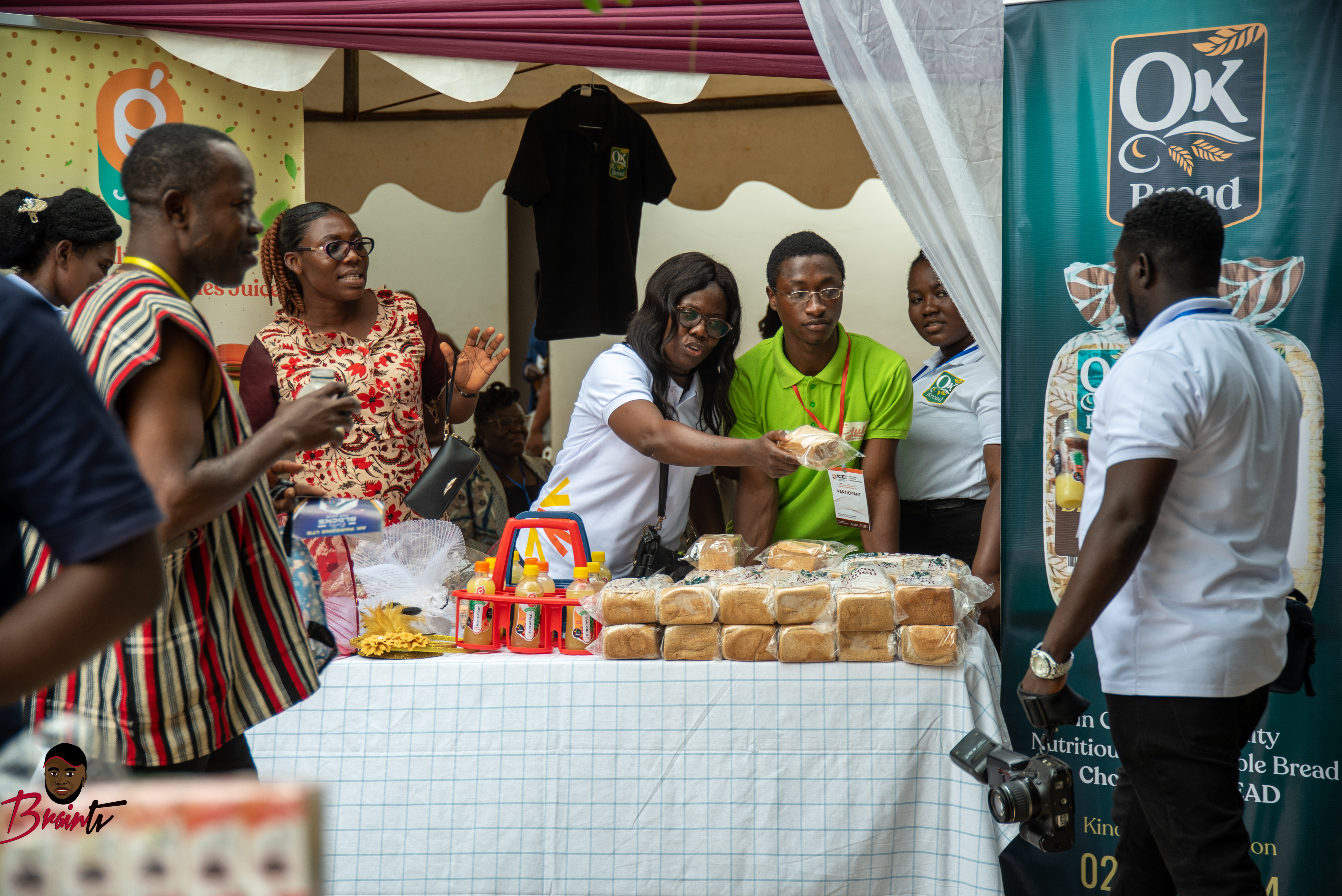 Outdoor community outreach under a canopy: staff and neighbors gathered around a table with bread and drinks, representing direct social impact in the field.